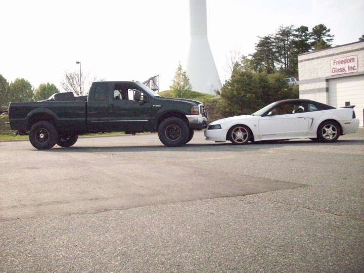 White 2000 Ford Mustang parked next to a dark green Ford F-250 truck, side view