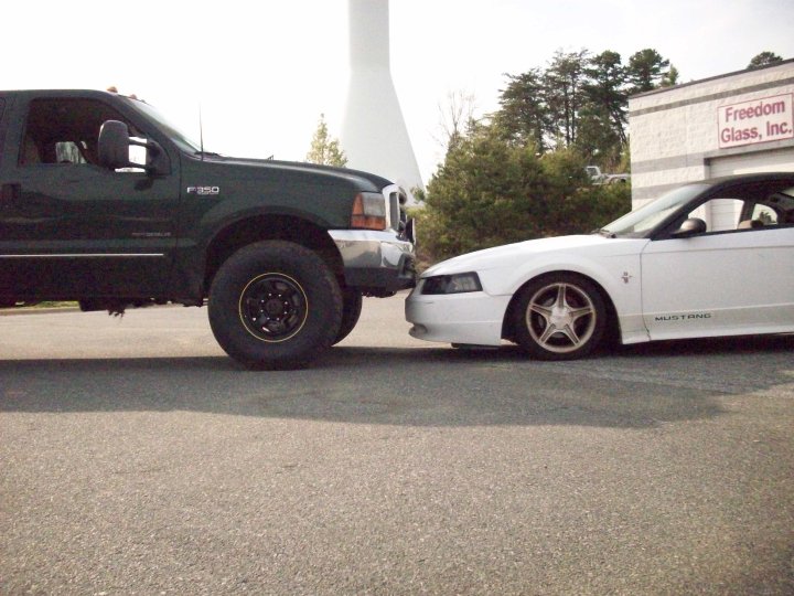 White 2000 Ford Mustang side view, bumper to bumper with a dark green Ford F-350 truck