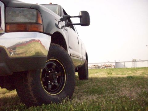 2000 Ford F-350 - A dark gray 2000 Ford F-350 truck is seen from a low angle, parked on a grassy field under a bright sky.