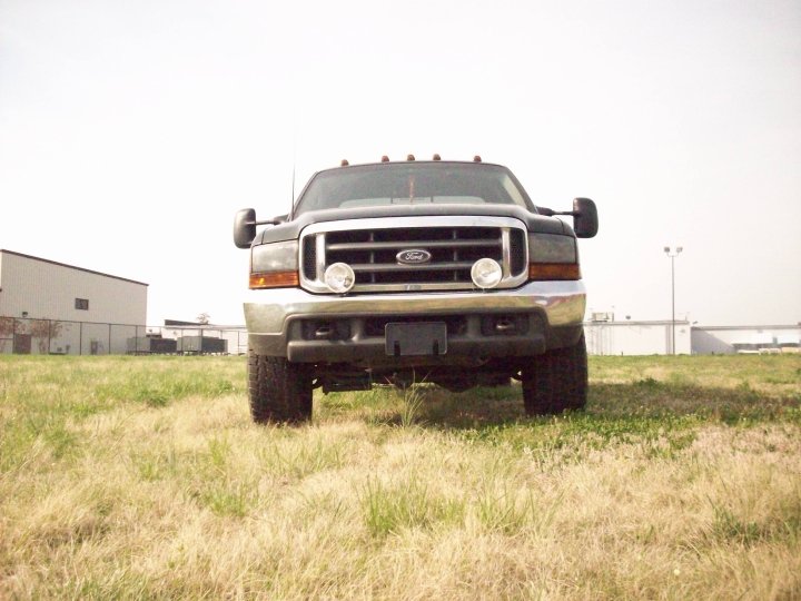 Dark gray Ford F-350 truck front view, parked on dry grass in front of industrial buildings