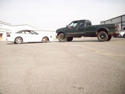2000 Ford F-350 - A dark green Ford F-350 pickup truck is parked on asphalt next to a white convertible.