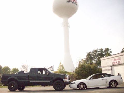 2000 Ford F-350 - A dark green Ford F-350 pickup truck is parked next to a white Ford Mustang, with a water tower in the background.