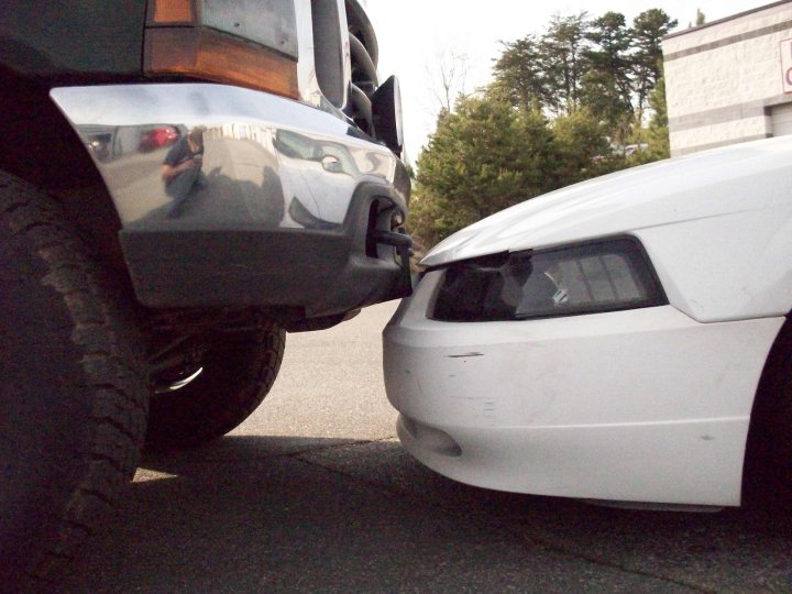 Front view of a white Ford Mustang bumper touching a chrome bumper of a dark-colored Ford F-350