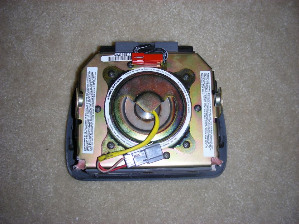 Airbag module with yellow wire and connectors, on a carpeted surface
