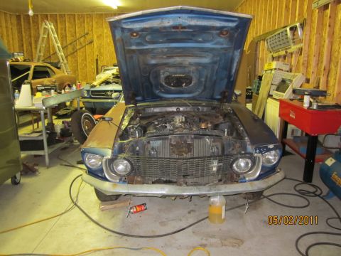1969 Ford Mustang - A blue 1969 Ford Mustang sits in a garage with its hood open, showing the engine bay. Another car is visible in the background.