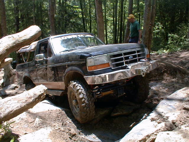 Lifted black Ford Bronco on big mud tires flexing over rocks on a forest off-road trail