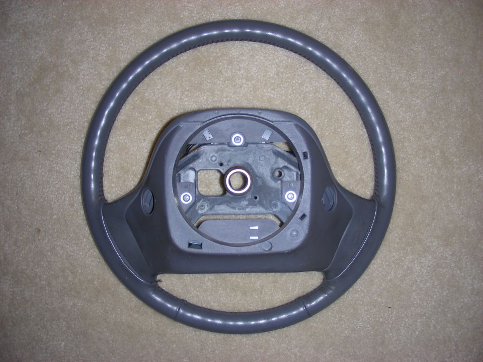 Gray steering wheel with dark gray plastic center hub, on a carpeted surface