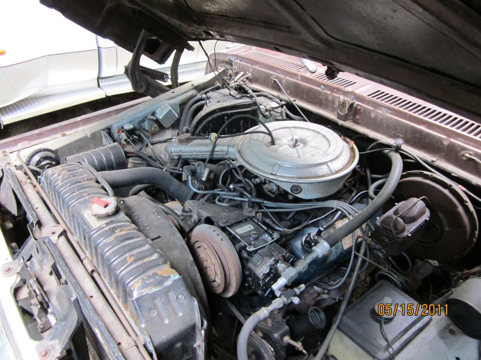 Engine bay with V8 engine, radiator, and air cleaner assembly. Brown vehicle exterior visible