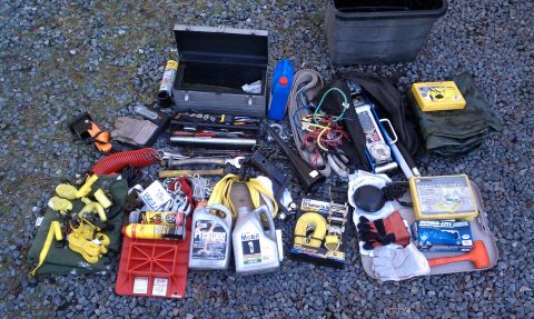 1979 Ford Bronco - A variety of tools and vehicle recovery equipment, such as a toolbox, jack, and tow straps, are spread out on a gravel surface.