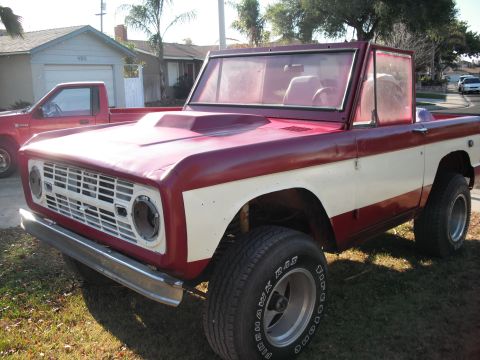 1968 Ford Bronco - A two-tone red and white Ford Bronco is parked in a grassy yard with a red pickup truck behind it.