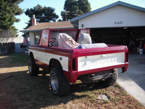 1968 Ford Bronco - A red and white 1968 Ford Bronco is parked in a yard with its doors open.