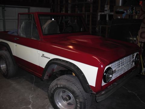 1968 Ford Bronco - Passenger-side 3/4 front view of a freshly painted topless early Bronco in a garage, finished in deep red with a white bodyside sweep and s…