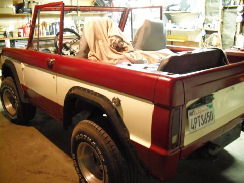 1968 Ford Bronco - Three-quarter rear view of a red-and-white early Ford Bronco sitting topless in a workshop, with a California plate reading 4PTS650 on the…