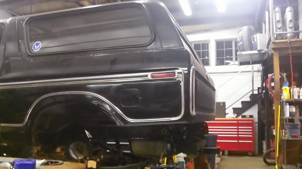 Black Ford Bronco in a garage, rear quarter view. It's on a lift with tools and shelves in the background