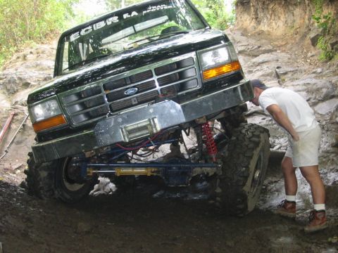 1994 Ford Bronco - A black 1994 Ford Bronco navigates a challenging rocky off-road trail with a person inspecting the front.
