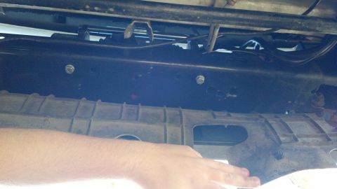 1996 Ford Bronco - Underside view of a vehicle's chassis components, with a hand reaching near the plastic trim.