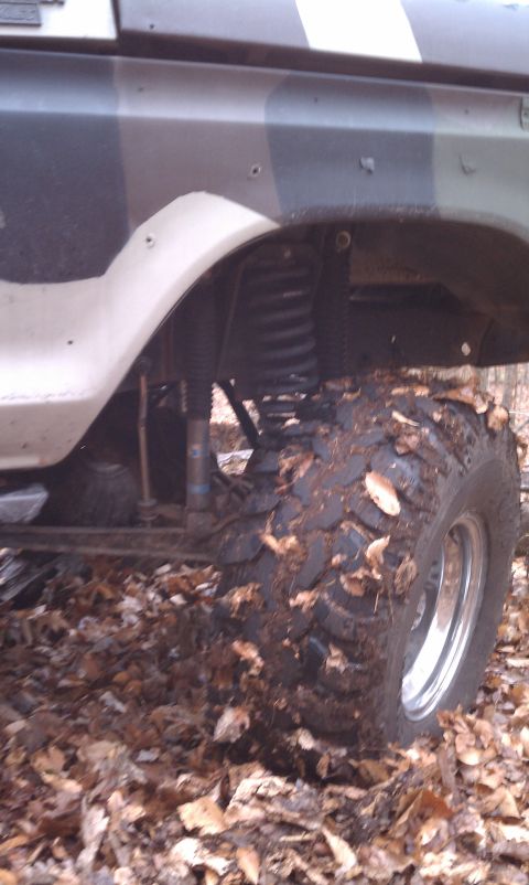 1979 Ford Bronco - Side view of a camouflaged off-road vehicle with large tires and visible suspension components.