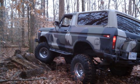 1979 Ford Bronco - This lifted SUV with a camouflage paint job navigates a challenging wooded trail.