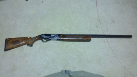 2010 Champion 188 - A shotgun with detailed engraving on its receiver is displayed on a textured surface.