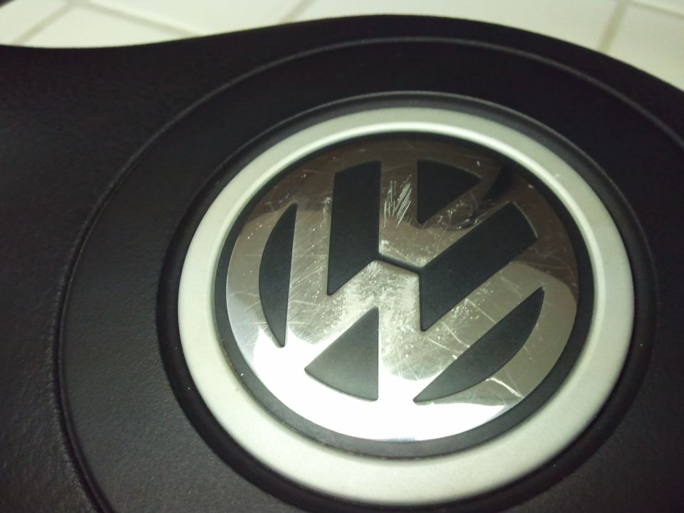 Close-up of a scratched Volkswagen emblem on a black steering wheel
