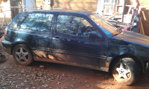 1991 Ford Festiva - Side view of a dark blue hatchback, covered in mud and debris.