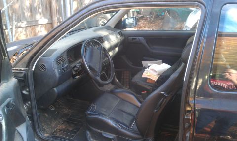 1991 Ford Festiva - The interior of a dark-colored Volkswagen Golf shows a worn dashboard and seats, with papers on the passenger seat.