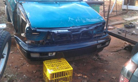 1991 Ford Festiva - Car front end is damaged and missing its grille, propped up by a yellow crate.