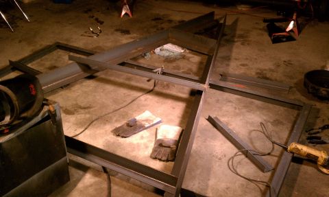 1990 Ford Bronco - A metal frame is being constructed on a concrete floor, with welding tools and protective gloves nearby.