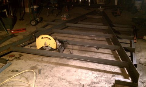 1990 Ford Bronco - A metal frame, likely for a trailer, is under construction with a chop saw nearby on the concrete floor.