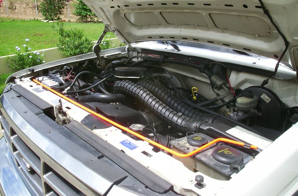 Engine bay of a white Ford Bronco with hood open, orange prop rod across radiator support