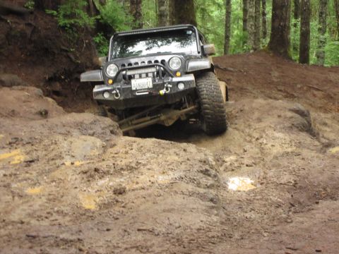 2008 Jeep Wrangler - A black 2008 Jeep Wrangler tackles a challenging muddy incline on a wooded trail.