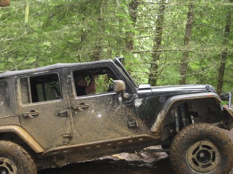 2008 Jeep Wrangler - A black Jeep Wrangler navigates a muddy off-road trail surrounded by dense forest foliage.