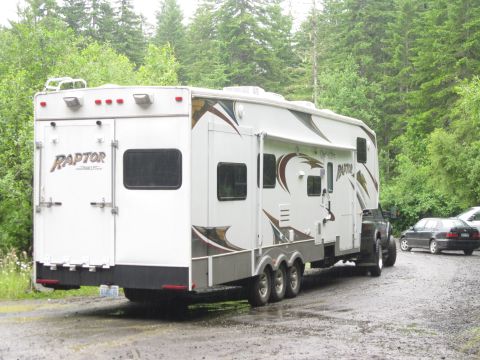 2008 Jeep Wrangler - A white Raptor fifth wheel RV trailer is parked on a gravel road, with a car visible in the background.