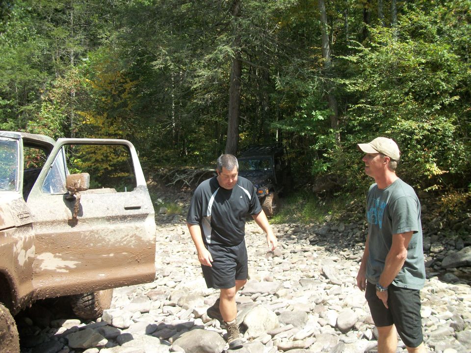 Muddy 1977 Ford F-150 with door open, and another off-road vehicle behind it. Two men stand on rocky ground