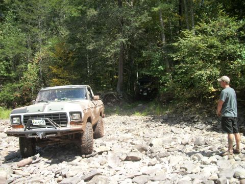 1979 Ford Bronco - A 1979 Ford F-150 pickup truck navigates a rocky path in a wooded area, with another vehicle visible in the background.
