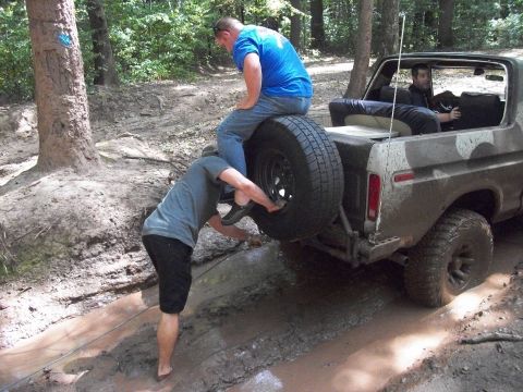 1979 Ford Bronco - A 1979 Ford Bronco with camouflage paint is stuck in a muddy trail, with two people attempting to free it.