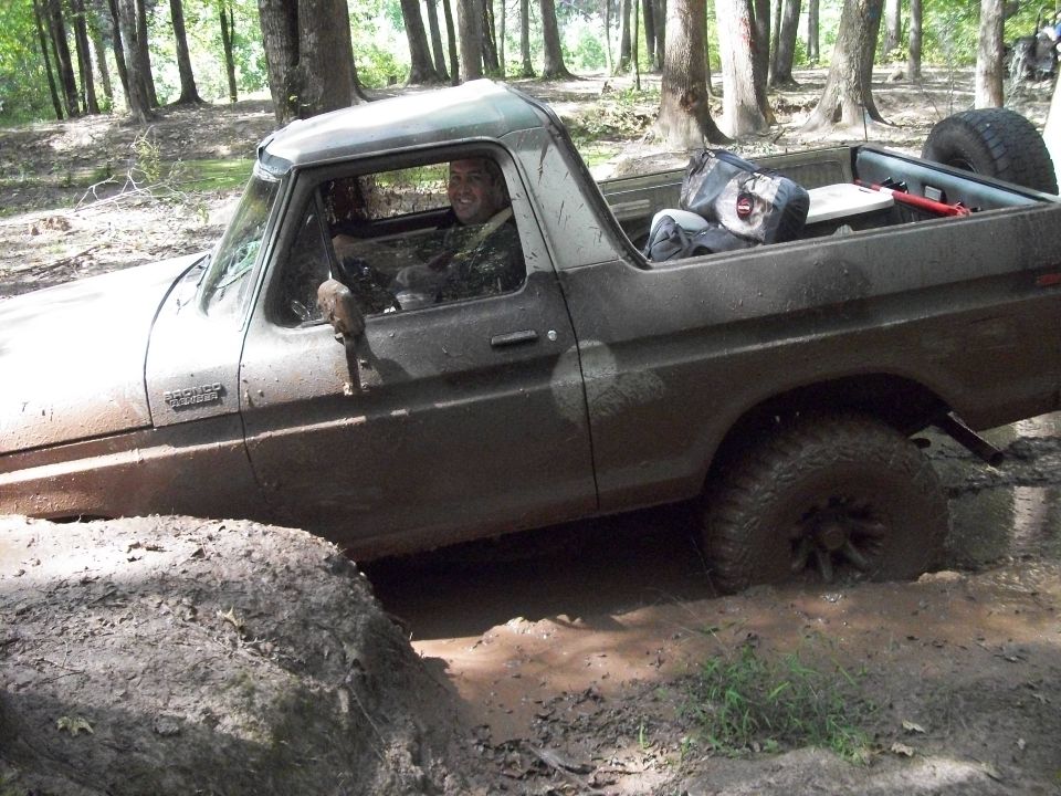 Mud-covered 1978 Ford Bronco stuck in a muddy ditch, driver visible through the window