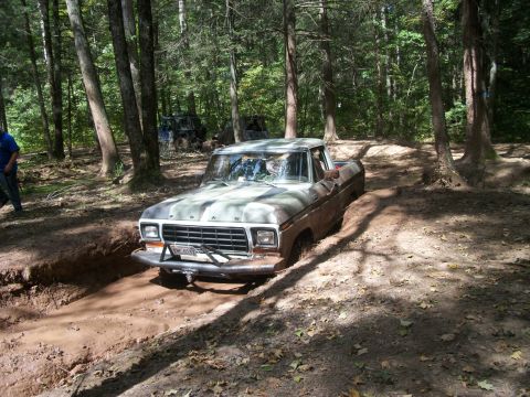 1979 Ford Bronco - Ford pickup truck stuck in mud off-road, with another vehicle in the background woods.