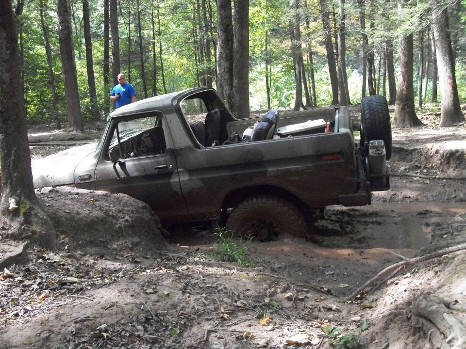 Ford Bronco stuck deep in mud with a person standing nearby in the woods