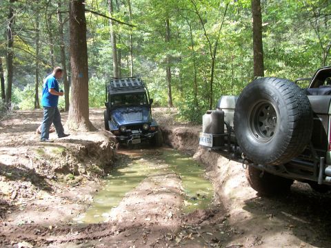 1979 Ford Bronco - Two off-road vehicles navigate a challenging muddy path in a wooded area.