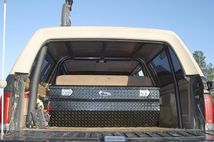 Rear cargo area of tan Bronco with black diamond-plate storage box and roll bar