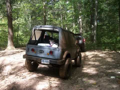 1979 Ford Bronco - Two off-road vehicles, a Suzuki Samurai and another SUV, navigate a wooded trail.