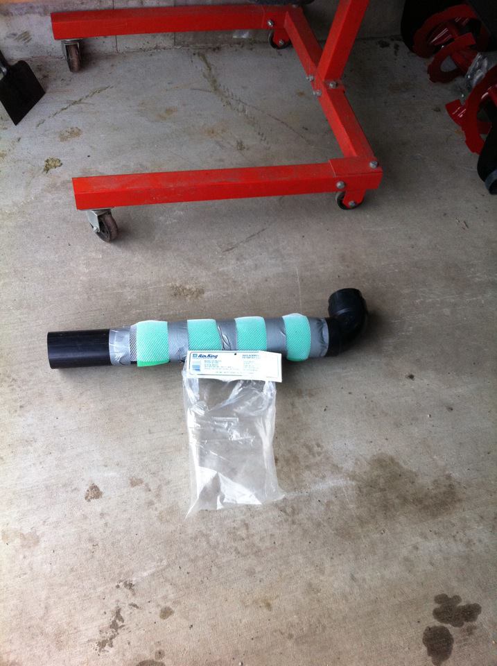 Exhaust pipe with green padding and a plastic bag of parts on a concrete floor