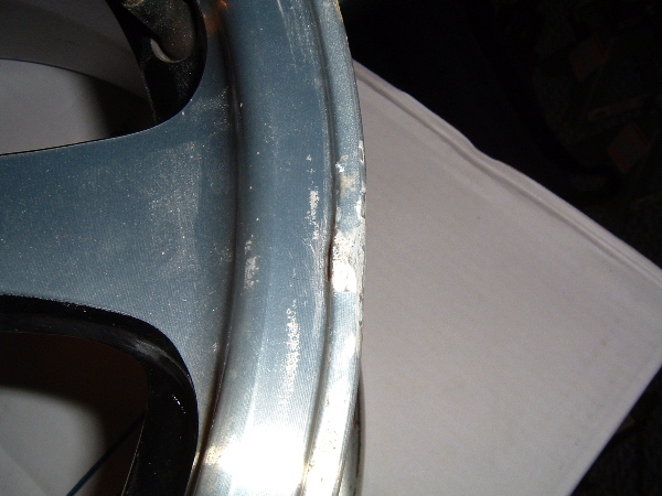 Close-up of a damaged blue wheel rim with chipped paint and curb rash