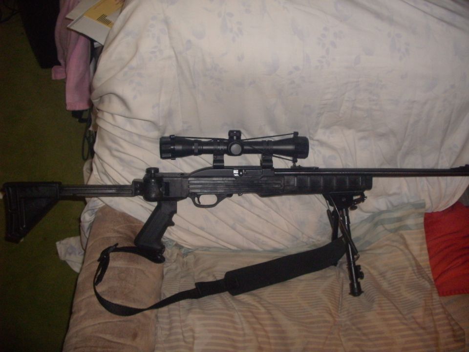 Black rifle with a scope mounted on top and a bipod attached to the front