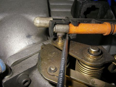 1990 Ford Bronco - A screwdriver is used to adjust the linkage on a vehicle's throttle body, connected by an orange cable.