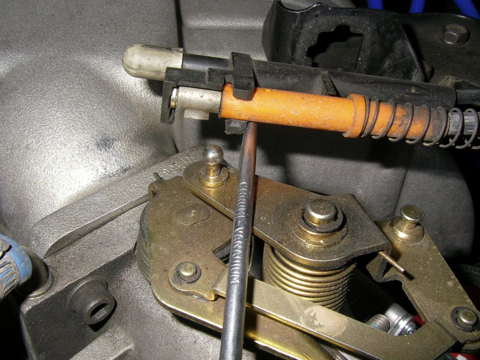 Throttle linkage with orange cable housing and metal components, a wrench is inserted