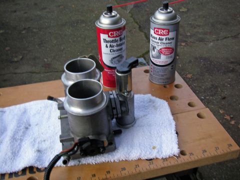 1990 Ford Bronco - Throttle body and two cans of CRC cleaner are laid out on a workbench for maintenance.