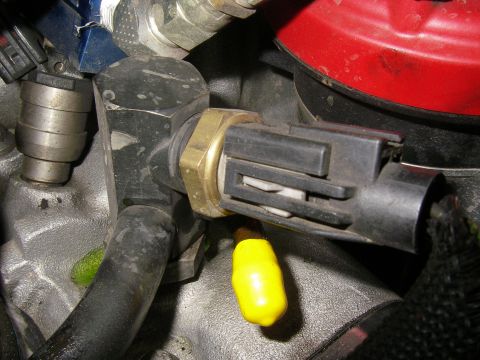 1990 Ford Bronco - Close-up of a brass-bodied coolant temperature sensor threaded into an aluminum housing with its gray two-pin connector plugged in, plus a…