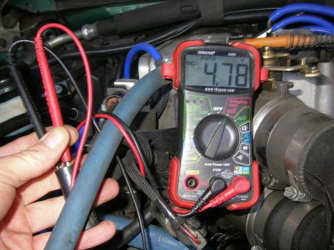 1990 Ford Bronco - A hand holds multimeter probes connected to engine components, displaying a reading of 4.78V DC.